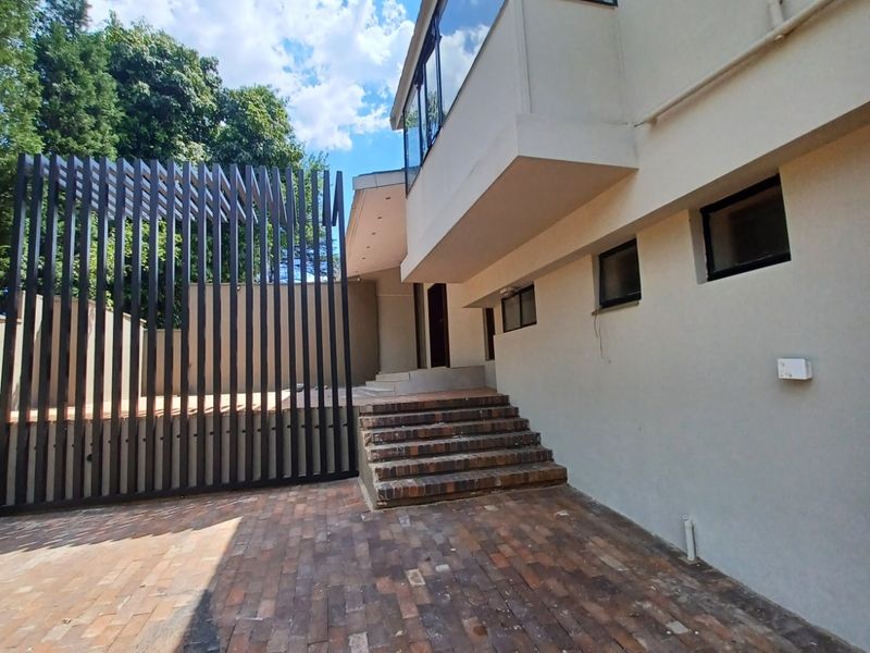 Rear exterior view featuring brick paved courtyard, vertical slat privacy screen, and brick steps leading to the building entrance.