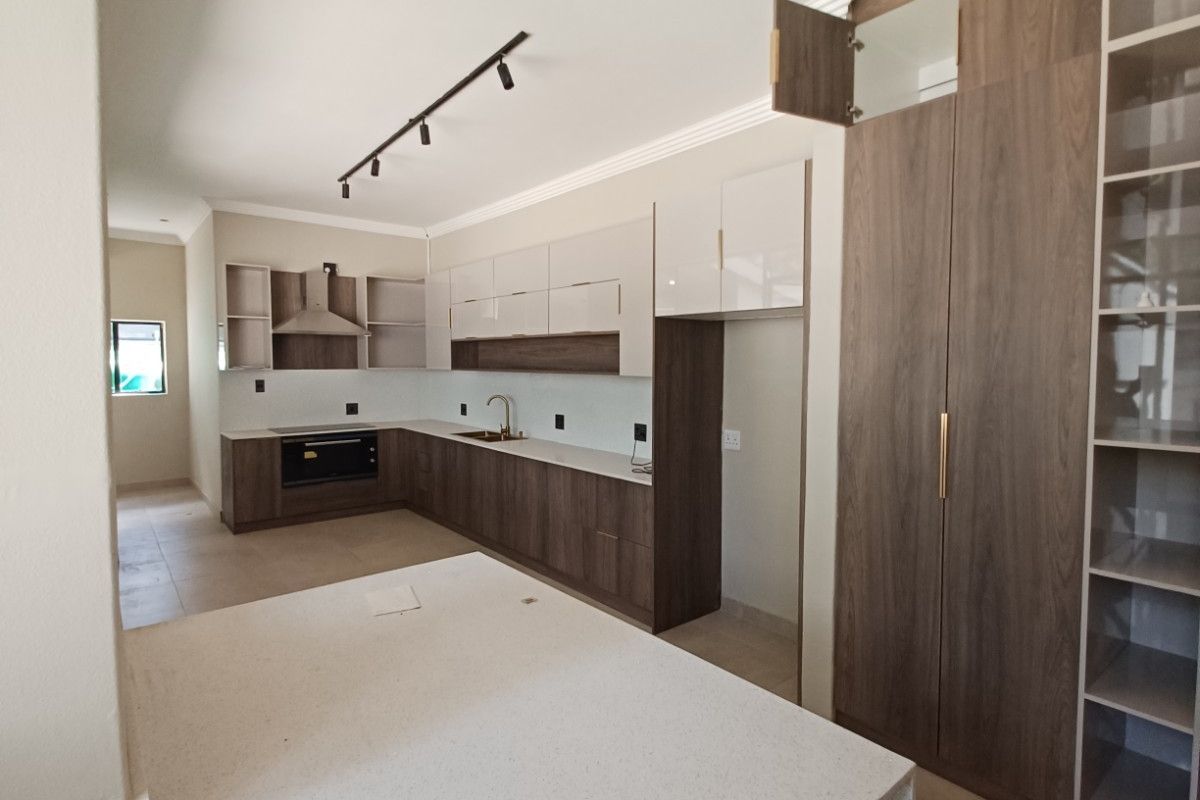 Modern kitchen featuring two-tone cabinetry, stone countertops, integrated oven, extractor fan, and ample storage space with a dedicated pantry unit.