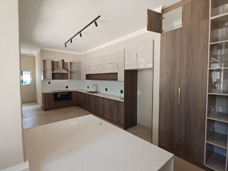 Modern kitchen featuring two-tone cabinetry, stone countertops, integrated oven, extractor fan, and ample storage space with a dedicated pantry unit.