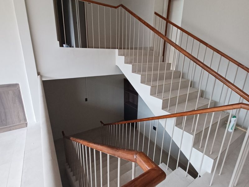 A bright, modern staircase featuring tiled steps, a sleek metal balustrade, and a polished wooden handrail, connecting multiple levels of the home.