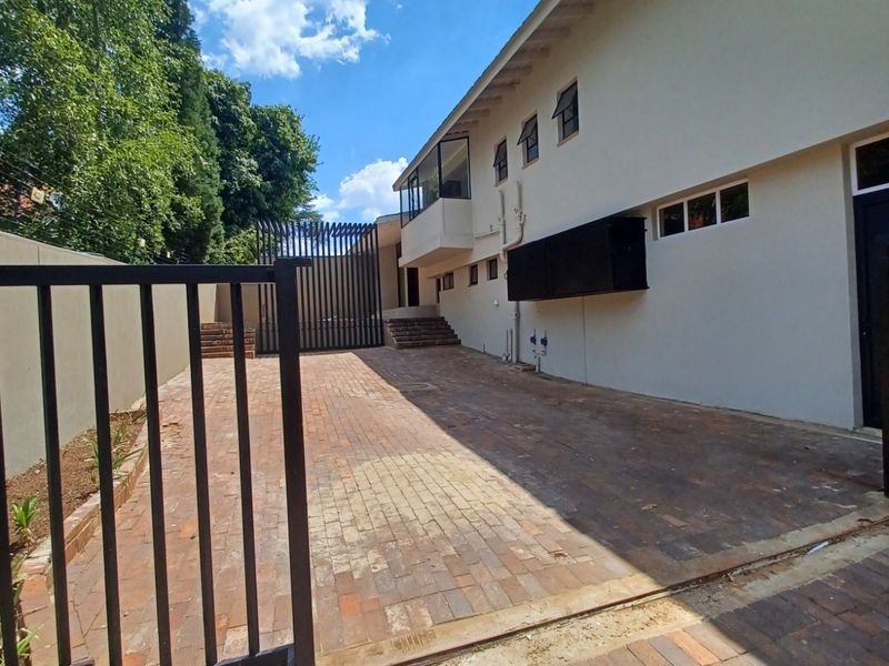 A paved driveway leading to a secure gated entrance with a multi-story building facade featuring casement windows and exterior wall finishes.