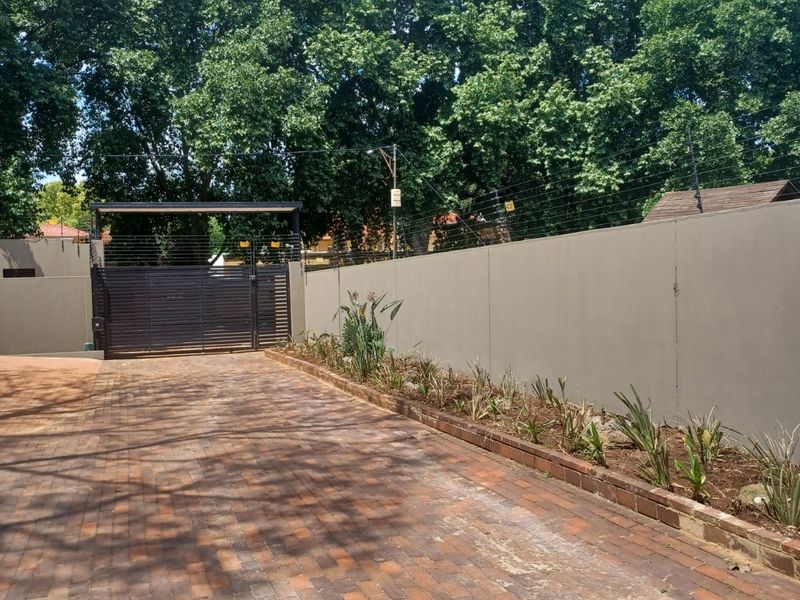 A secure front entrance featuring a paved driveway, perimeter wall with electric fencing, and a modern metal sliding gate.