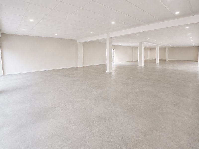A spacious, open-plan commercial interior featuring polished concrete flooring, a suspended ceiling with recessed lighting, and structural support columns.