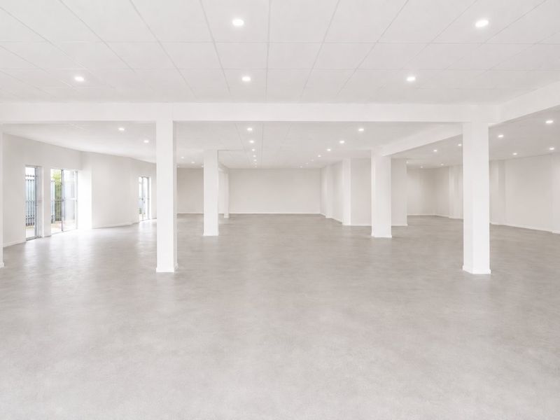 A spacious, open-plan commercial interior featuring polished concrete floors, structural support columns, and modern recessed ceiling lighting throughout the expansive area.