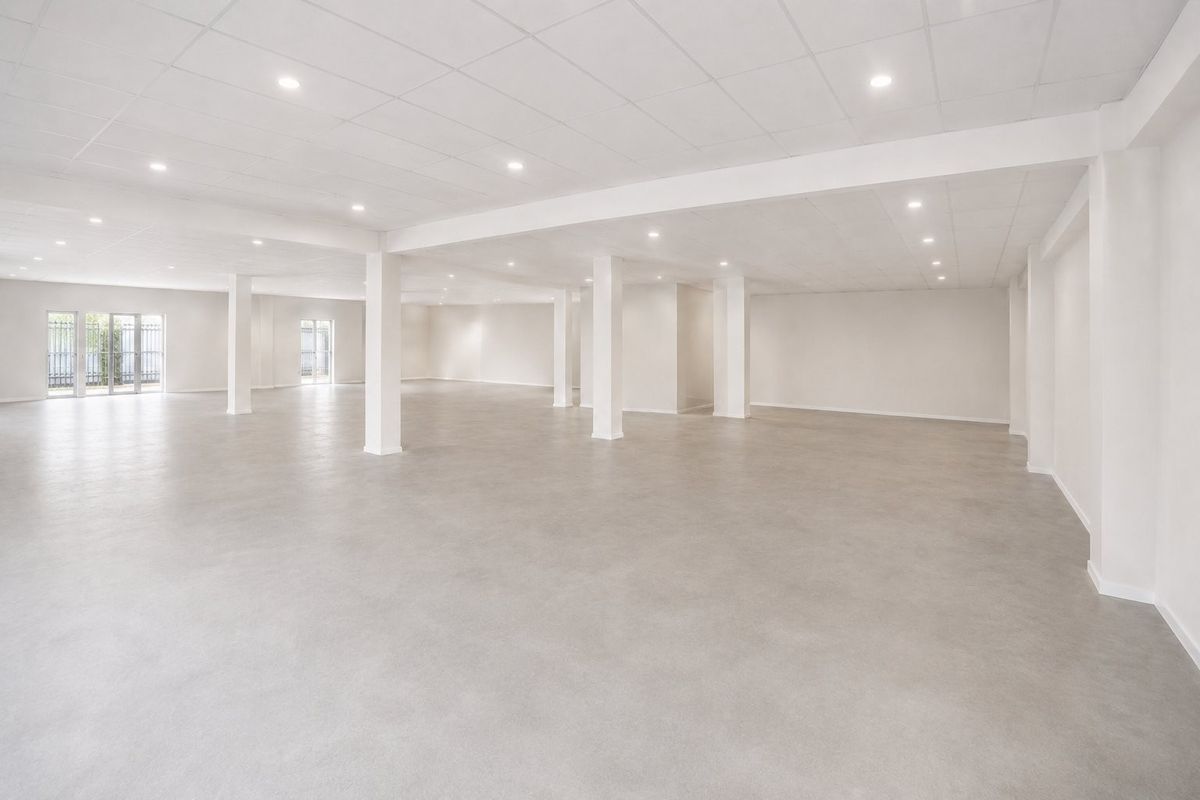 A spacious, open-plan commercial interior featuring polished concrete floors, a clean suspended ceiling with recessed lighting, and structural support columns.
