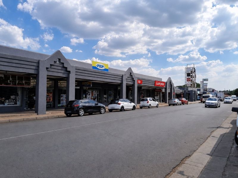 Street-level view of a commercial retail strip center featuring multiple storefronts with prominent signage and a paved pedestrian walkway.