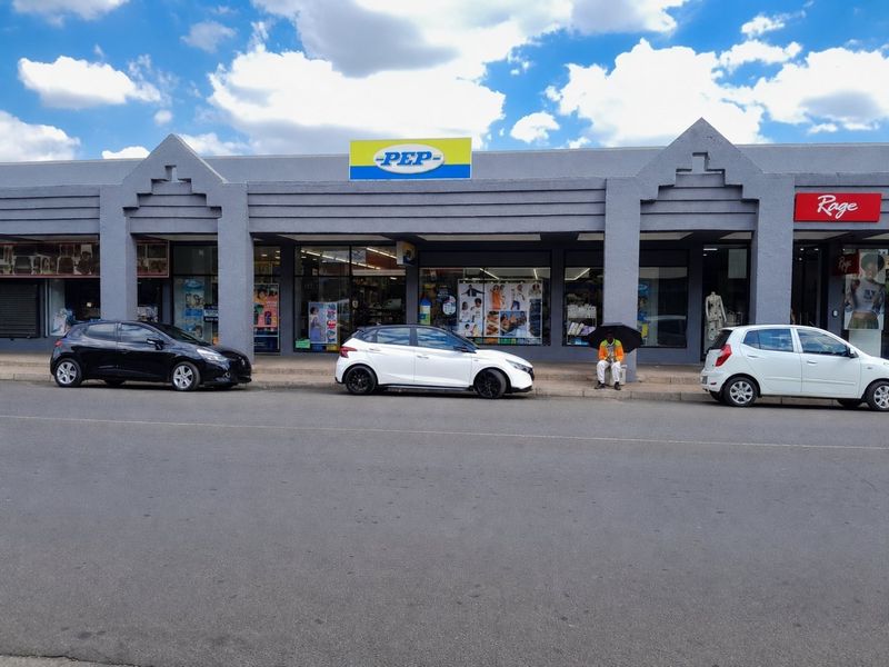 Front elevation of a commercial retail storefront featuring large display windows and prominent signage along a paved street.