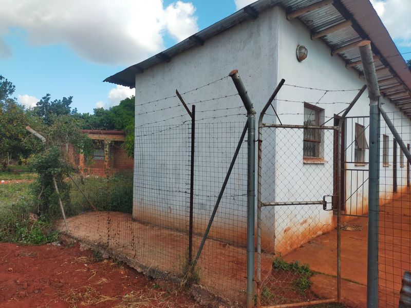 Exterior view of a commercial building featuring a corrugated metal roof, security fencing with barbed wire, and a gated entrance.