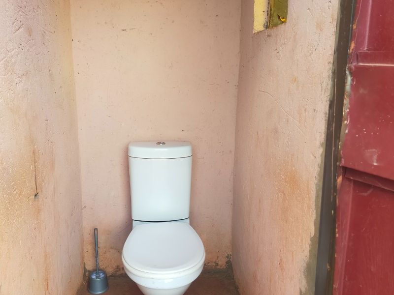 A small, basic bathroom facility featuring a standard toilet, requiring significant cosmetic updates and wall finishing to improve the overall condition.