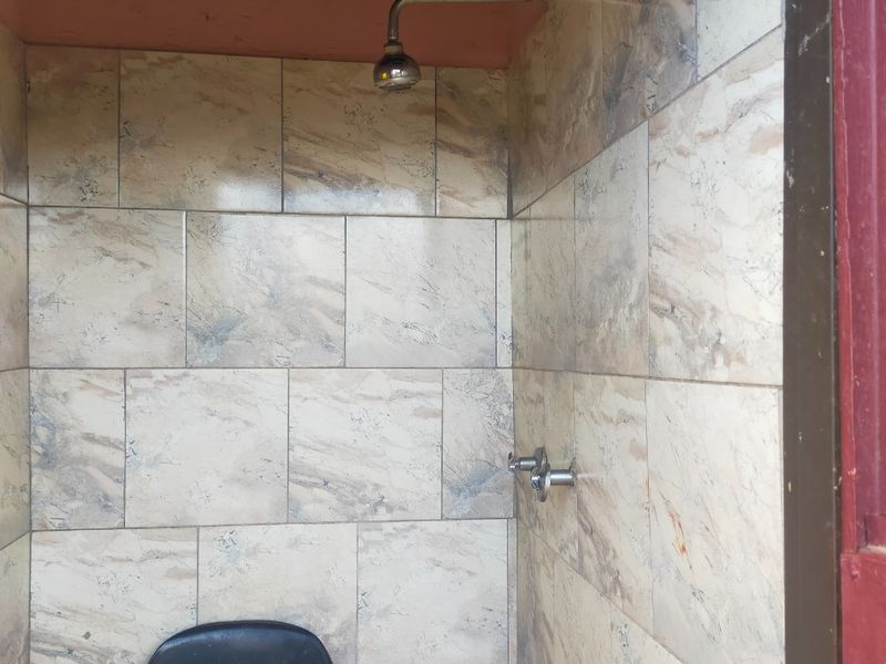 A basic shower stall featuring tiled walls and exposed plumbing, currently requiring ceiling repairs and general maintenance to improve the overall condition.