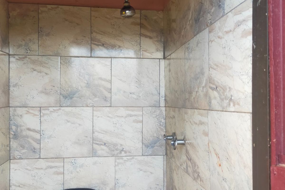 A basic shower stall featuring tiled walls and exposed plumbing, currently requiring ceiling repairs and general maintenance to improve the overall condition.