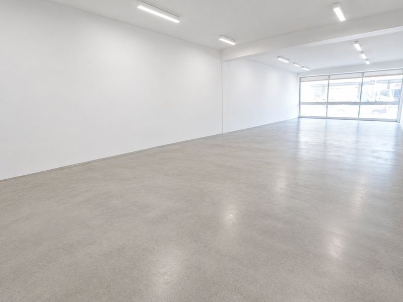 A spacious, open-plan commercial unit featuring polished concrete floors, bright overhead lighting, and a large glass storefront window providing ample natural light.