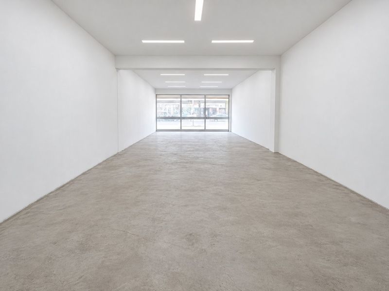 A bright, open-plan commercial space featuring polished concrete floors, recessed lighting, and a large glass storefront entrance, ideal for retail or office use.