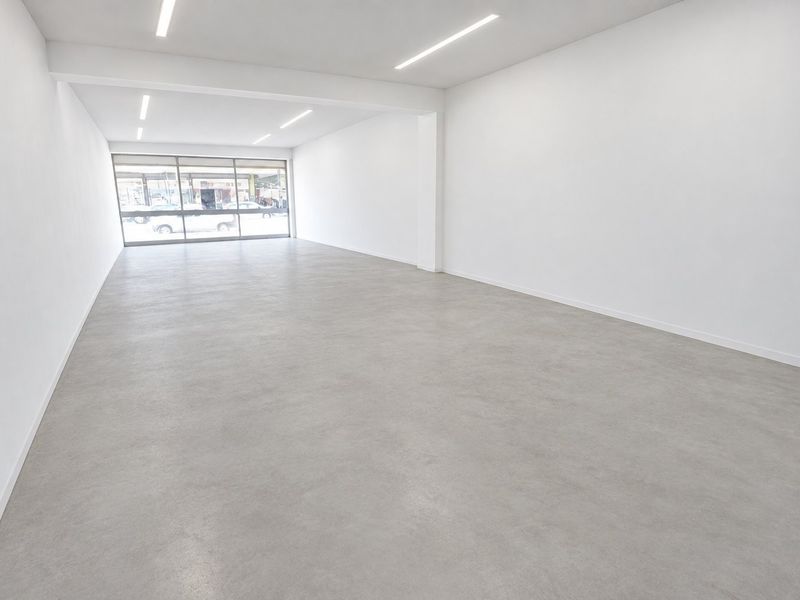 A bright, modern open-plan commercial space featuring polished concrete floors, recessed linear lighting, and a large glass storefront window providing excellent natural light.