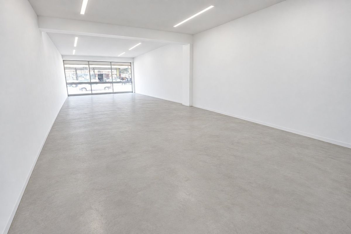 A bright, modern open-plan commercial space featuring polished concrete floors, recessed linear lighting, and a large glass storefront window providing excellent natural light.