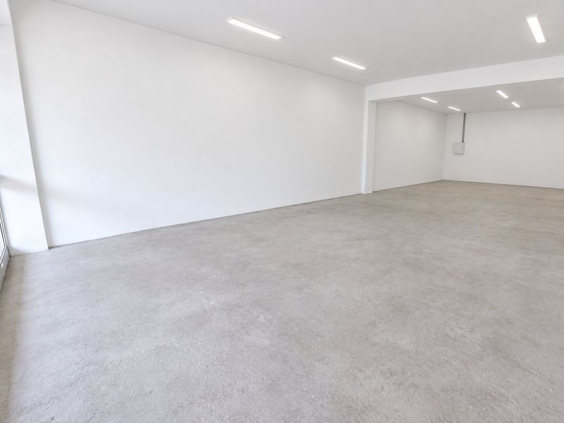 A bright, open-plan commercial space featuring polished concrete floors, recessed LED lighting, and a large glass storefront window, ideal for retail or office use.