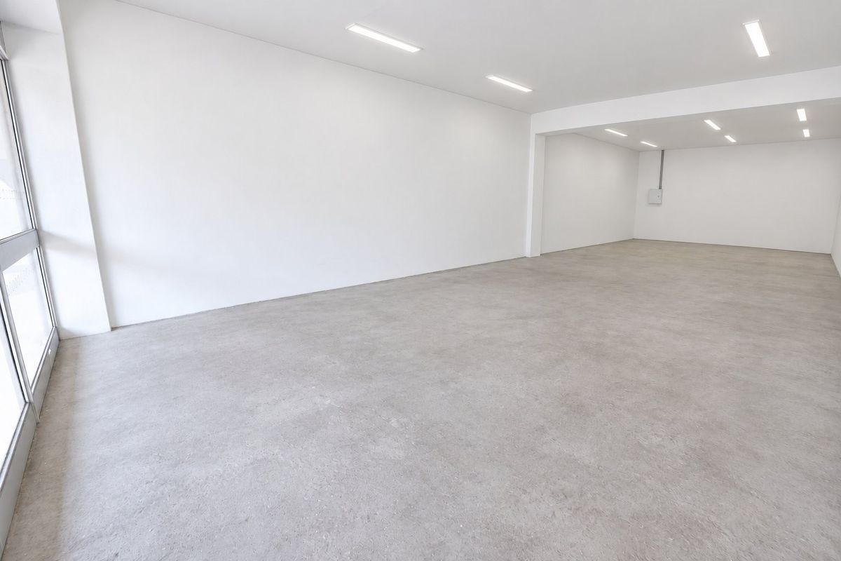 A bright, open-plan commercial space featuring polished concrete floors, recessed LED lighting, and a large glass storefront window, ideal for retail or office use.