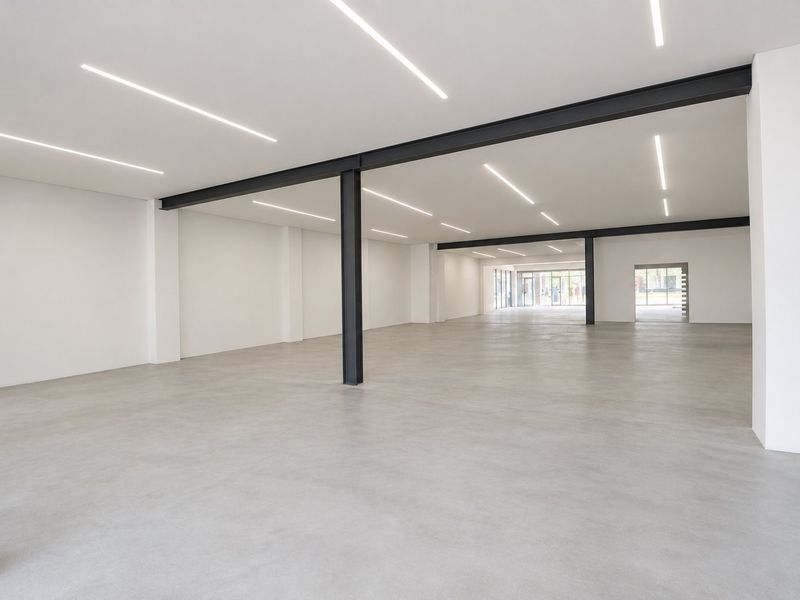 A spacious, modern open-plan commercial area featuring polished concrete floors, exposed steel structural beams, and sleek recessed linear lighting throughout.