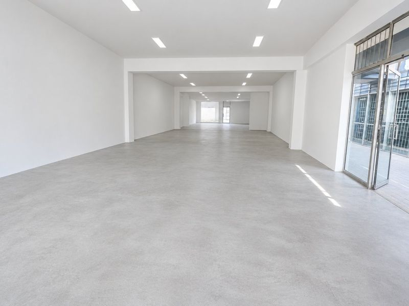 Spacious, open-plan commercial unit featuring polished concrete floors, recessed ceiling lighting, and a large glass entrance door with security gate.