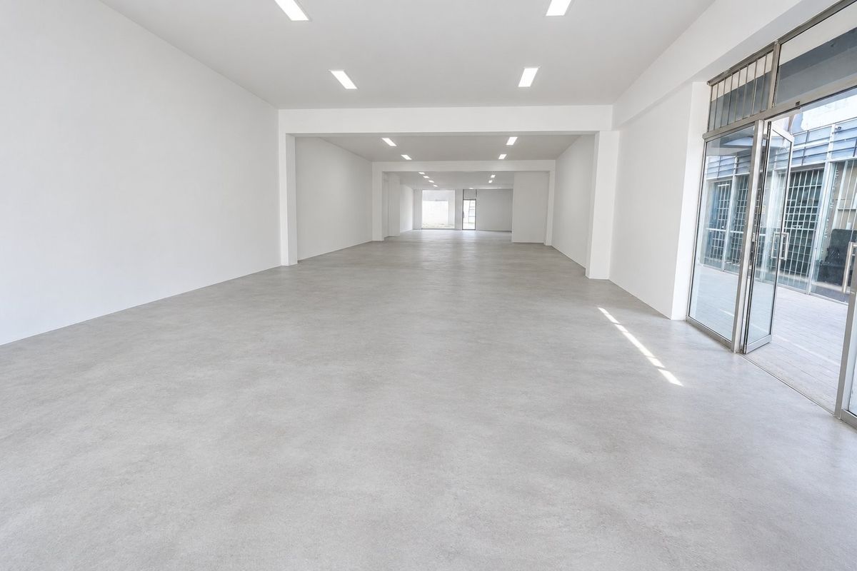 Spacious, open-plan commercial unit featuring polished concrete floors, recessed ceiling lighting, and a large glass entrance door with security gate.