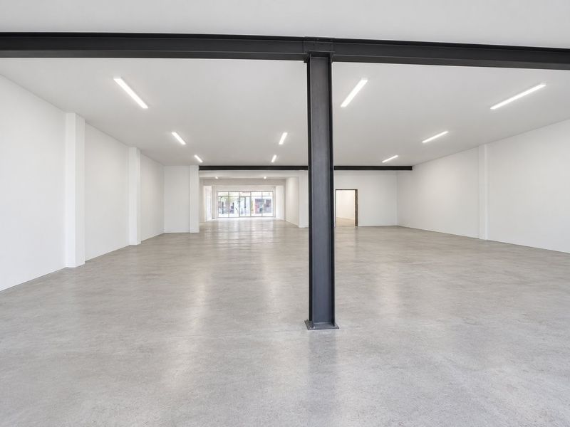 A spacious, modern open-plan commercial unit featuring polished concrete floors, exposed steel structural beams, and bright recessed lighting, ideal for retail or office use.