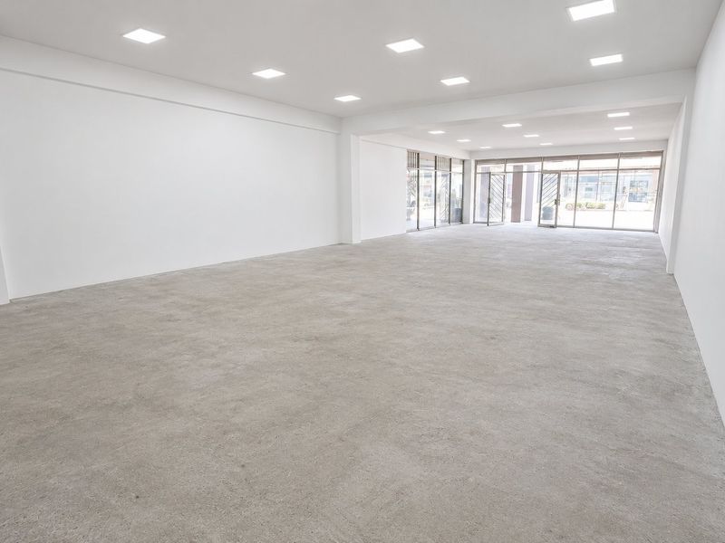 A spacious, open-plan commercial unit featuring polished concrete floors, recessed ceiling lighting, and large glass storefront windows providing ample natural light.