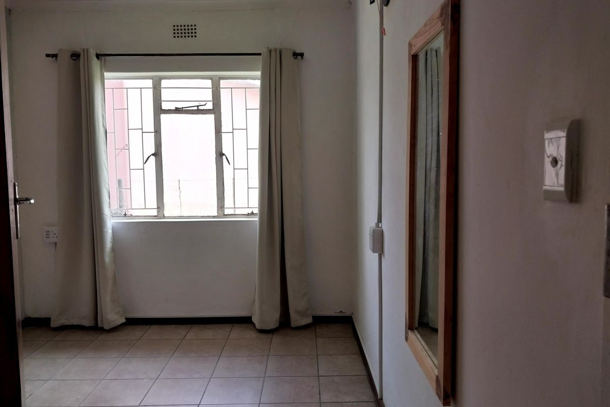 A simple, empty bedroom featuring tiled flooring and a window with security bars, providing a blank canvas for personalization.