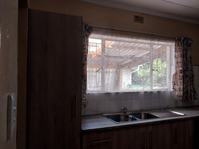 A functional kitchen area featuring a double bowl stainless steel sink, laminate countertops, and built-in cabinetry with a tiled splashback.