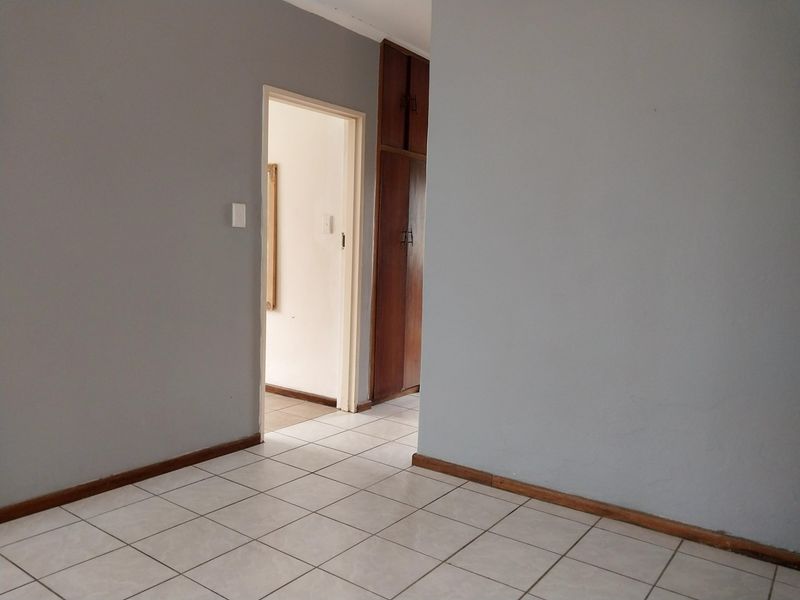 A vacant hallway featuring neutral grey walls, ceramic floor tiling, and built-in wooden storage cupboards.