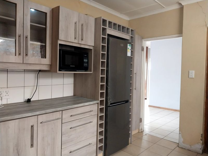 Kitchen featuring light wood-look cabinetry, laminate countertops, built-in microwave, and integrated wine rack, with tiled flooring and backsplash.