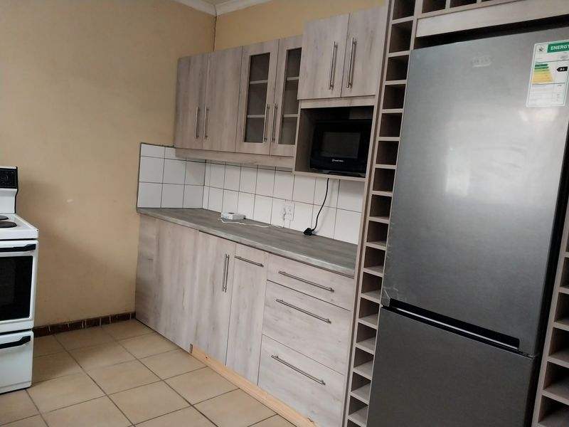 A functional kitchen featuring light wood-grain cabinetry, tiled backsplash, built-in microwave, and integrated wine storage, with ceramic floor tiles throughout.