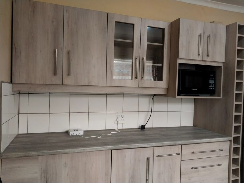 A functional kitchen area featuring light wood-look cabinetry, a tiled backsplash, laminate countertops, and a built-in microwave space with an integrated wine rack.