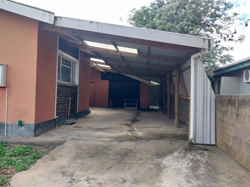 A rear exterior view showing a concrete driveway covered by a basic timber and corrugated metal carport structure attached to the house.