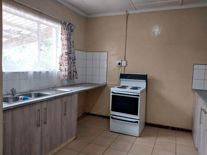 A functional kitchen featuring tiled flooring, built-in cabinetry, a stainless steel sink, and a freestanding stove, with potential for cosmetic updates.