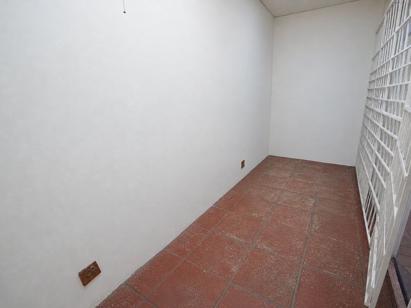 A vacant utility space featuring terracotta floor tiles and a secure metal gate, suitable for storage or a functional work area.