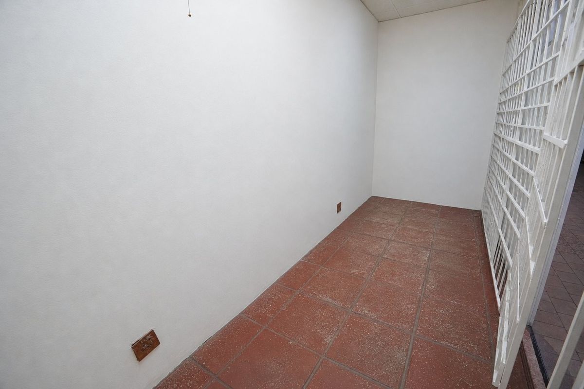 A vacant utility space featuring terracotta floor tiles and a secure metal gate, suitable for storage or a functional work area.
