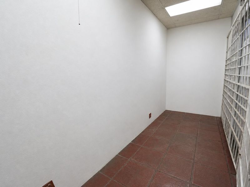 A vacant commercial office space featuring durable ceramic tile flooring, a drop ceiling with recessed lighting, and a secure metal gate entrance.