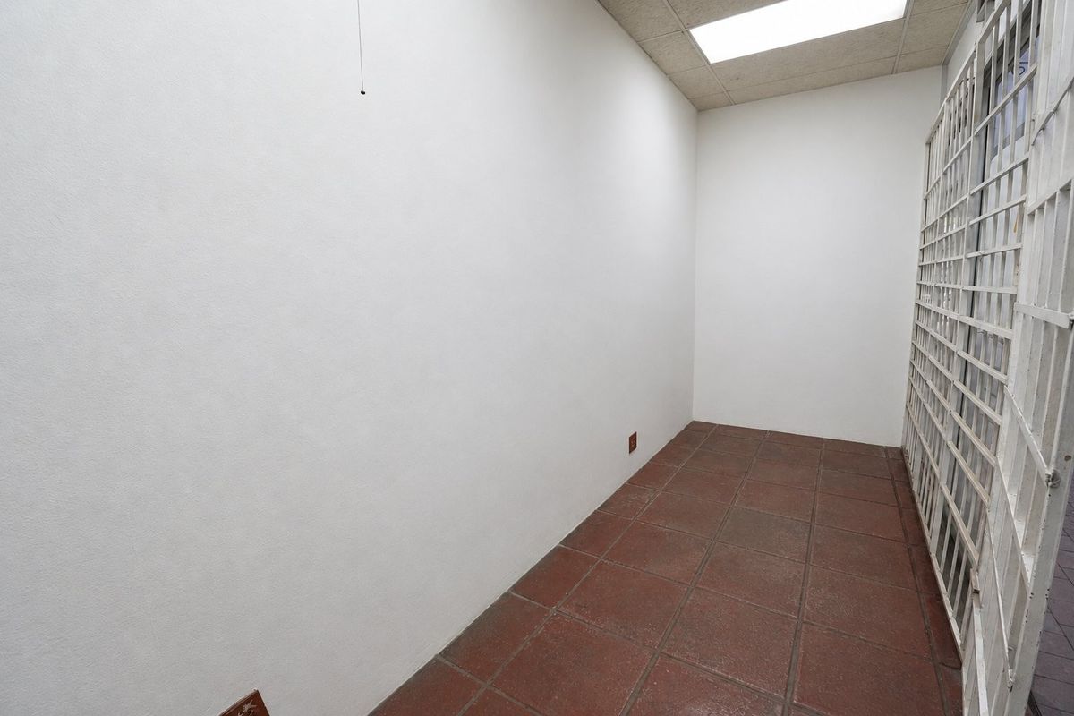 A vacant commercial office space featuring durable ceramic tile flooring, a drop ceiling with recessed lighting, and a secure metal gate entrance.