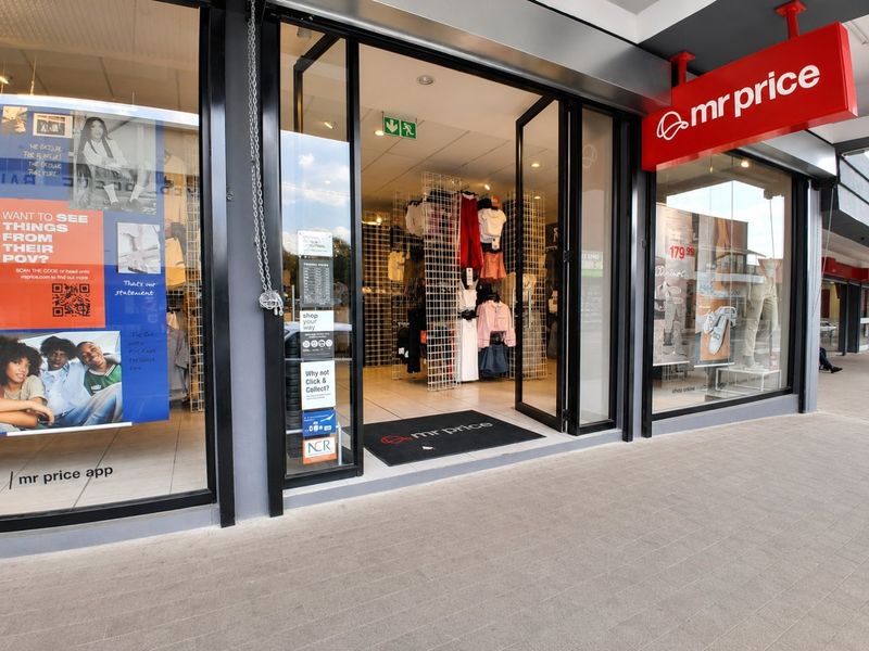 Commercial storefront entrance featuring large glass display windows, modern aluminum framing, and clear signage for a retail clothing outlet.
