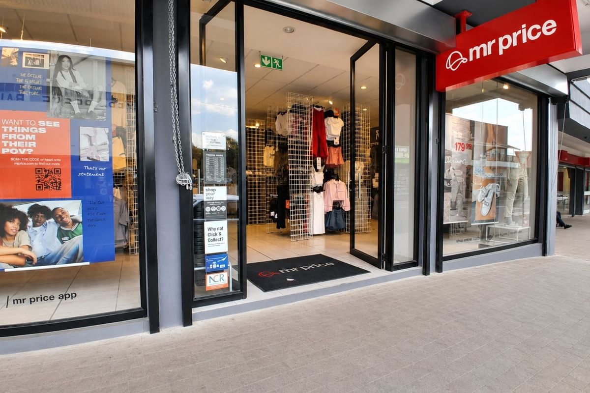 Commercial storefront entrance featuring large glass display windows, modern aluminum framing, and clear signage for a retail clothing outlet.