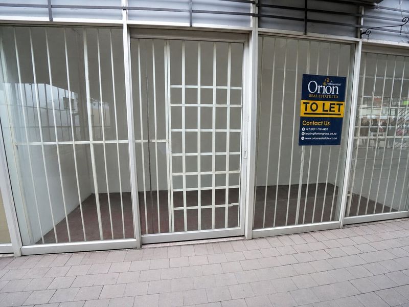 Commercial storefront featuring large glass windows with security bars, suitable for retail or office use, located on a paved street level.