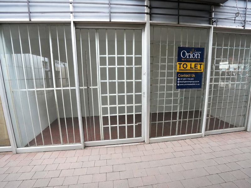 Commercial storefront featuring large glass windows with security bars and paved exterior access, currently available for lease.
