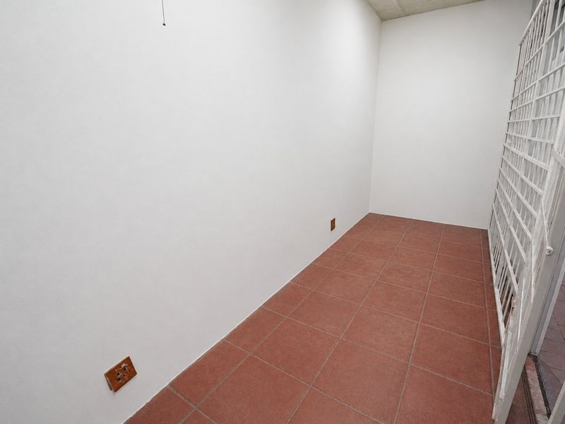A clean, empty utility space featuring durable tiled flooring, a secure metal gate, and functional electrical points, suitable for storage or workspace.
