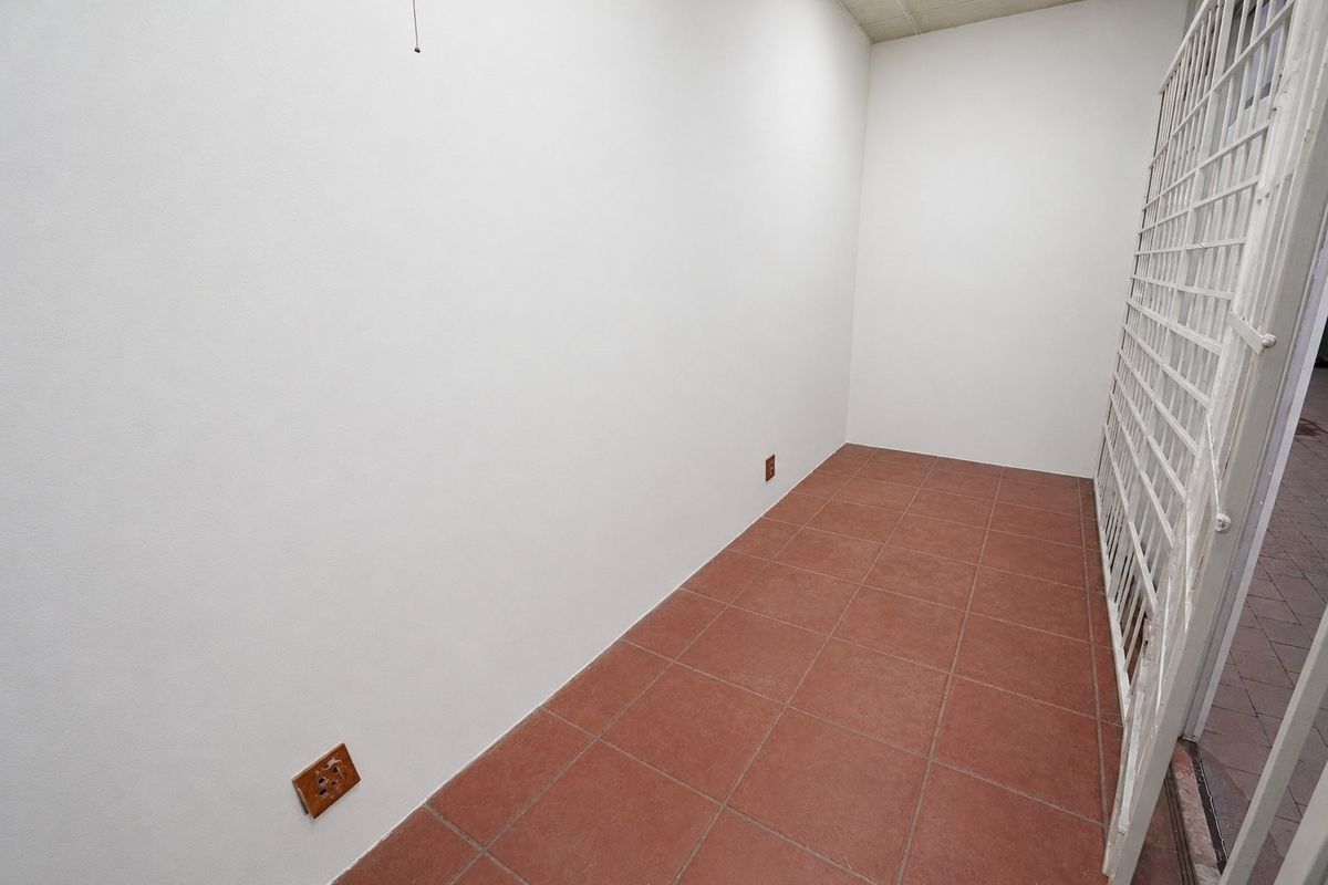 A clean, empty utility space featuring durable tiled flooring, a secure metal gate, and functional electrical points, suitable for storage or workspace.