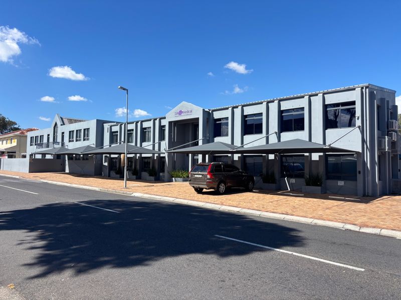 A professional multi-story office building featuring a paved parking area with shade sail carports and a modern grey facade.