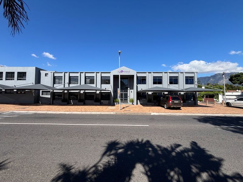 Front elevation of a modern commercial office building featuring paved parking, shade cloth carports, and a central glass entrance.