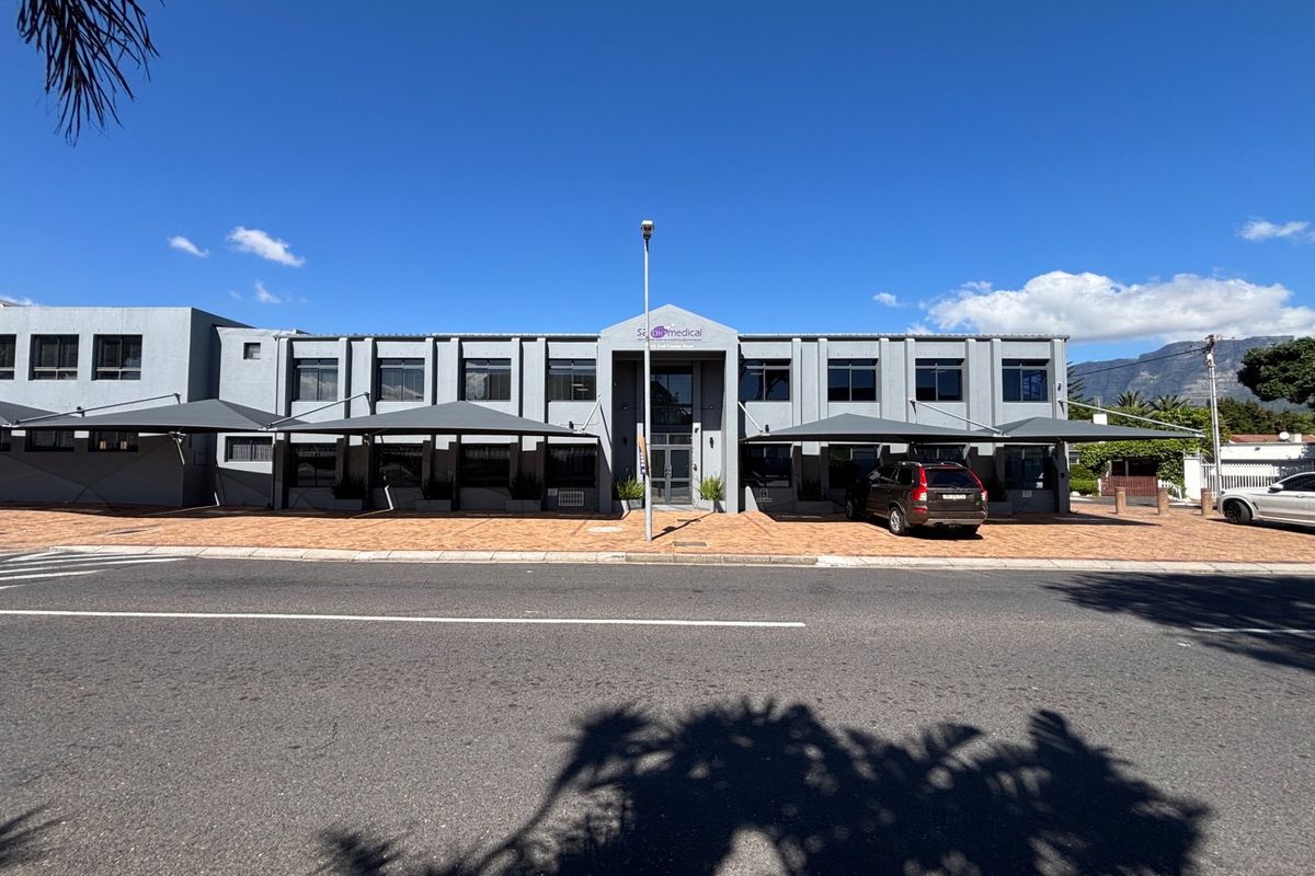 Front elevation of a modern commercial office building featuring paved parking, shade cloth carports, and a central glass entrance.