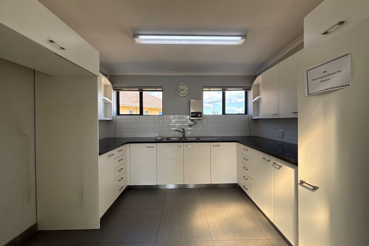 A clean, functional office kitchen featuring white cabinetry, dark countertops, subway tile backsplash, and tiled flooring, providing a practical space for staff use.