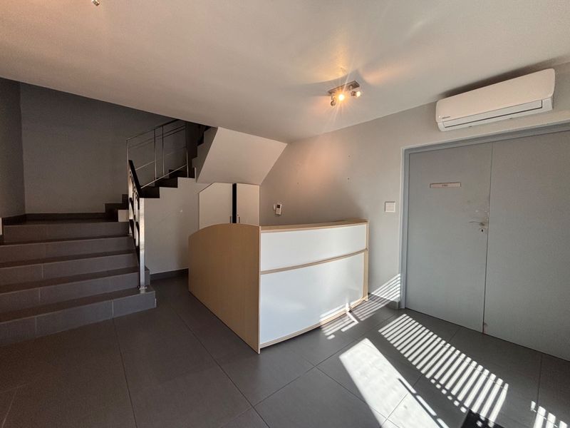 A modern office entry area featuring a built-in reception desk, tiled flooring, a staircase with a metal handrail, and a wall-mounted air conditioning unit.