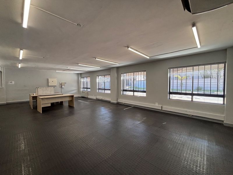 Spacious open-plan office area featuring durable rubber flooring, large windows with venetian blinds, and functional overhead fluorescent lighting.